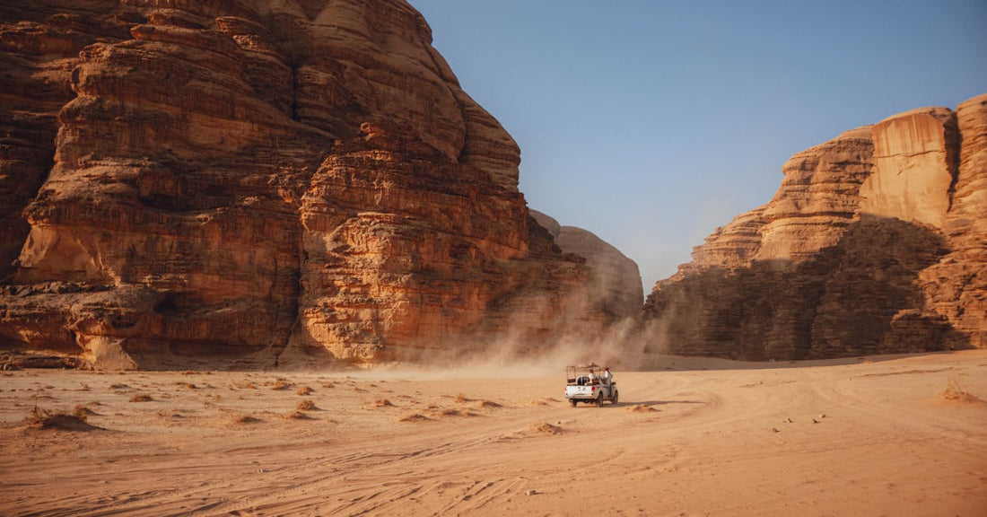 A compact car driving on a rough dirt road that is cutting through some large, green hills that stretch into the distance.